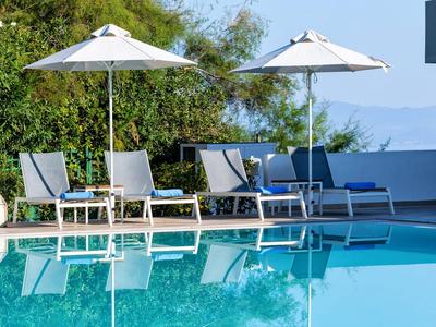 Vier Liegestühle mit weißen Sonnenschirmen am Rand eines klaren blauen Pools bei sonnigem Wetter.