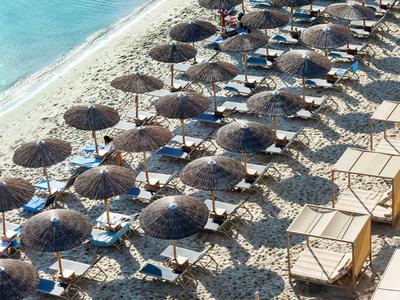 Beach with rows of sun umbrellas and lounge chairs beside clear blue water