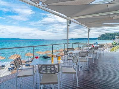 Restaurant terrace with tables and chairs by the sea under a sunshade.