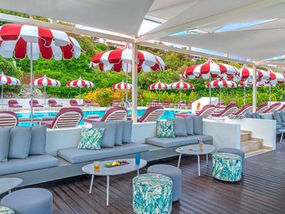 Modern lounge with gray sofas and colorful stools under red and white umbrellas.