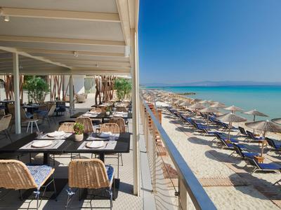 Taras restauracji na plaży z stołami, krzesłami i widokiem na leżaki na piaszczystej plaży i morze.