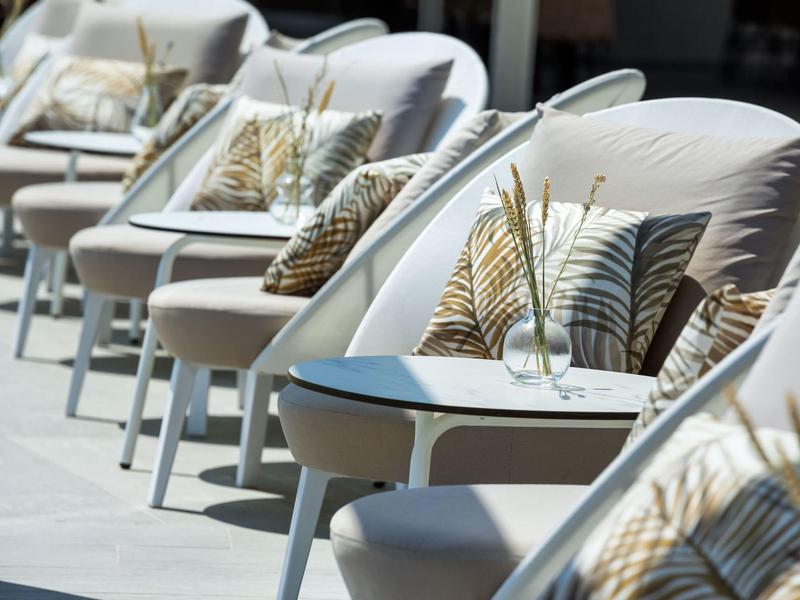 Row of comfortable lounge chairs with decorative pillows and small tables in an outdoor setting.