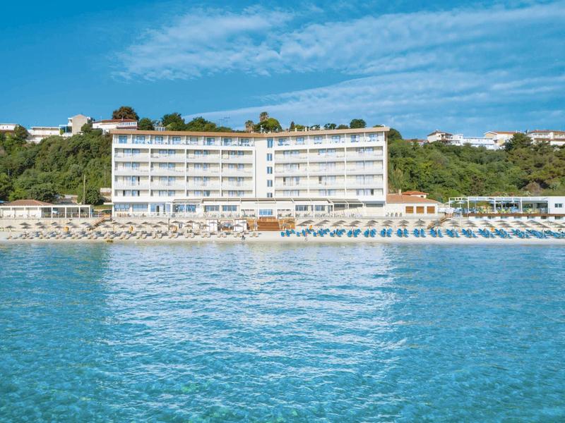 Hotel directly by the sea with sun umbrellas and loungers on the beach under a blue sky.