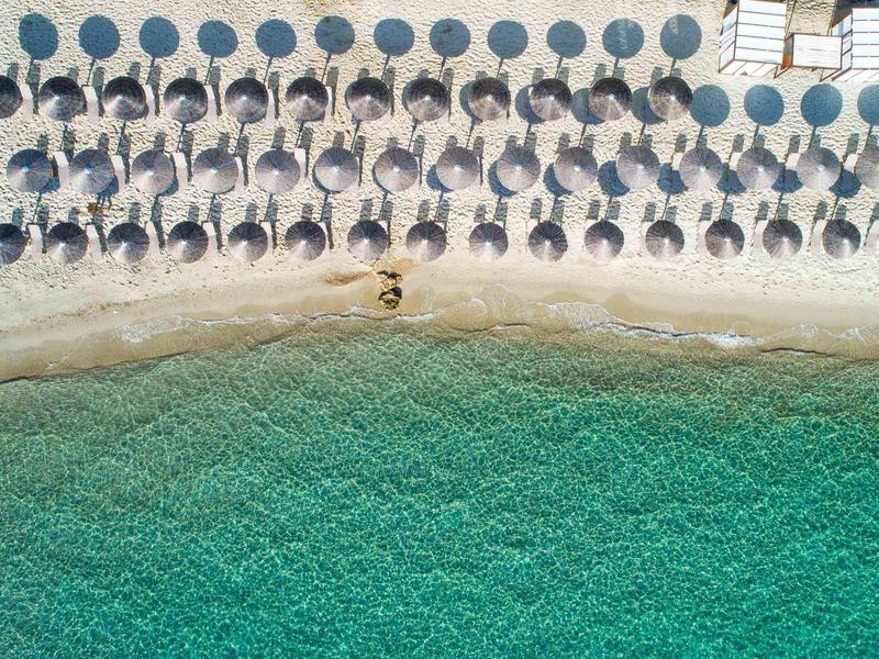Row of sun loungers with blue umbrellas on sandy beach by turquoise water