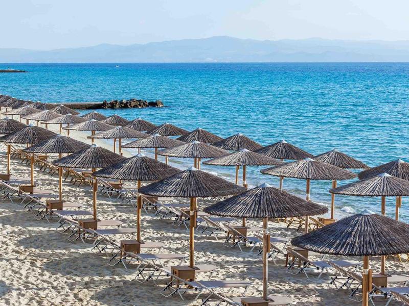 Row of umbrellas and sunbeds on sandy beach with view of calm blue sea.