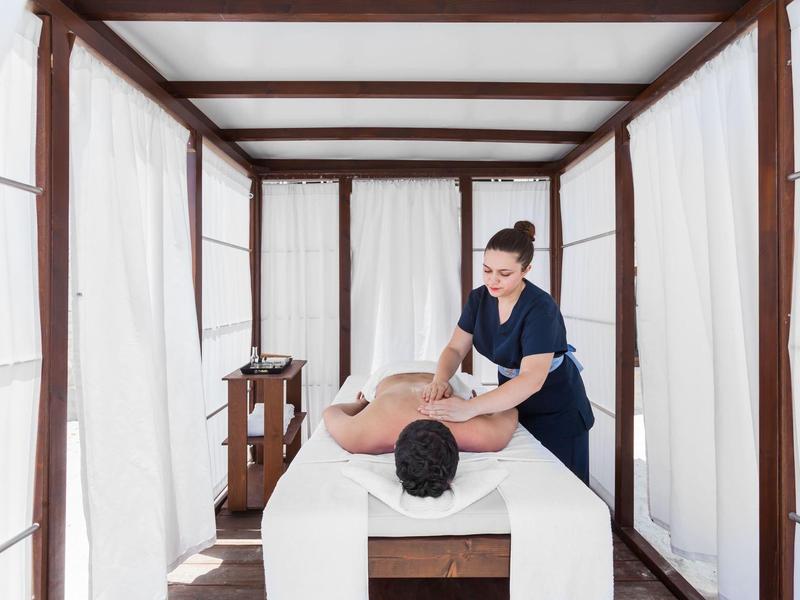 Masseuse treating a relaxed man in a bright, modern spa pavilion.