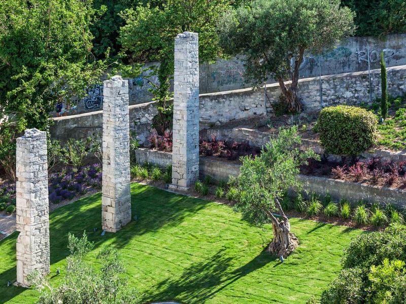 Three tall pillars on manicured grass with bushes and trees in the background.
