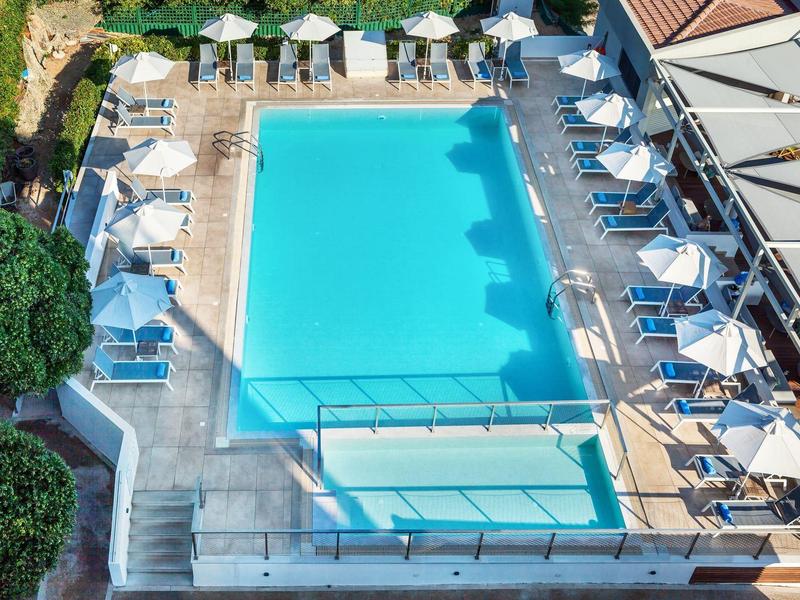 Rectangular and smaller pool with sun loungers and umbrellas in a hotel area.