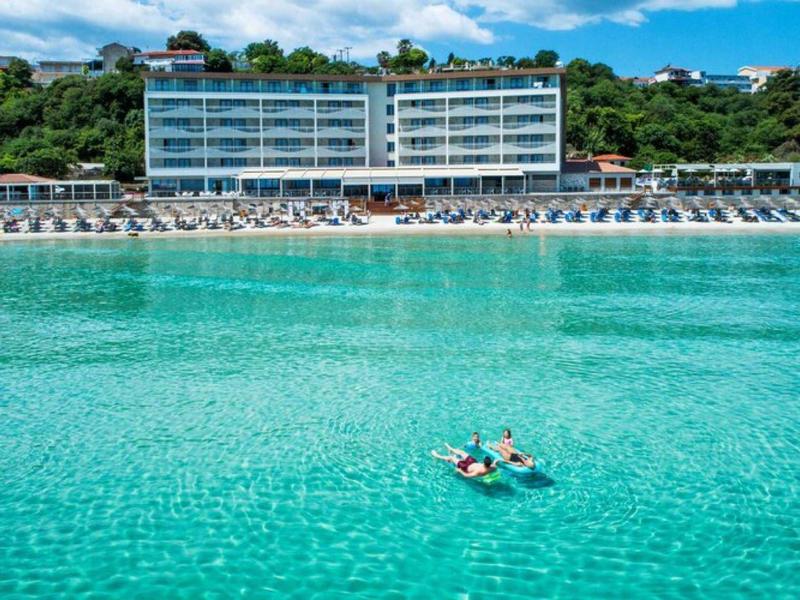 Modern hotel on the beach with clear turquoise water and two people in paddle boats.