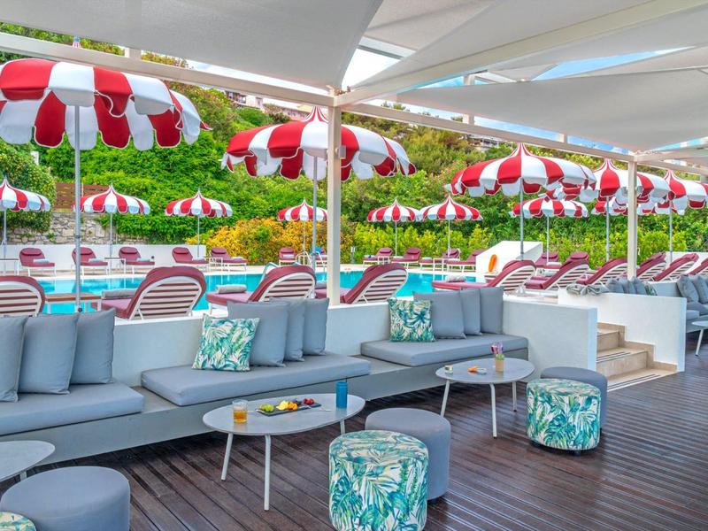 Modern lounge with gray sofas and colorful stools under red and white umbrellas.