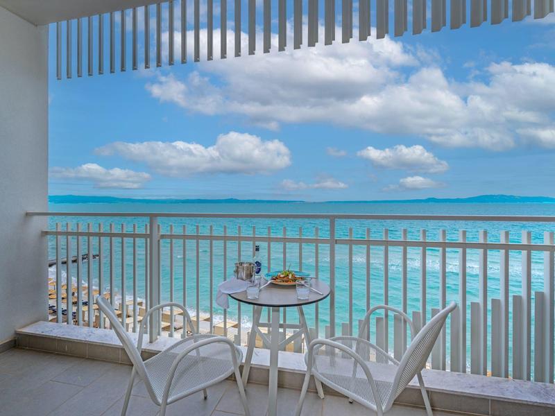 Balcony with table and two chairs overlooking the sea and cloudy sky.