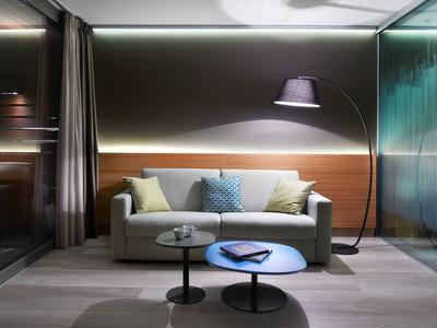 Modernes Wohnzimmer mit grauem Sofa, bunten Kissen und zwei runden Couchtischen, beleuchtet von Stehlampe.