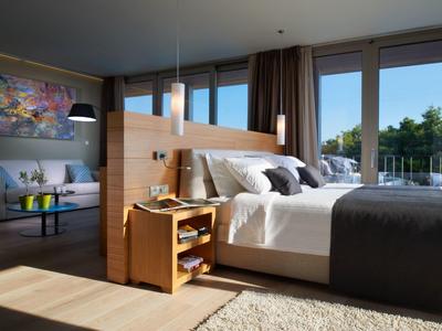 Helles Schlafzimmer mit großem Fenster, Holzmöbeln, weißen und grauen Betttextilien, und Teppichboden.