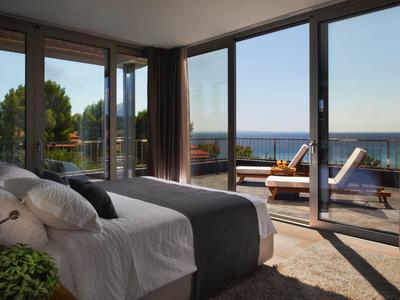 Hell eingerichtetes Schlafzimmer mit bodentiefen Fenstern und Terrasse mit Meerblick.