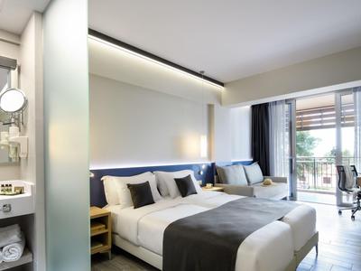 Modernes Hotelzimmer mit zwei Einzelbetten, Schreibtisch und Balkon mit Blick auf Bäume.