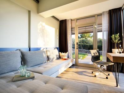 Helles Wohnzimmer mit grauem Ecksofa, Schreibtisch, Bürostuhl und Zugang zum Garten durch Glastüren.