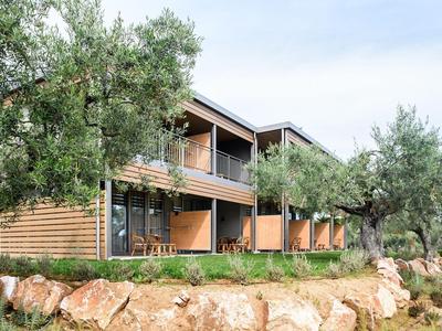 Modernes Hotelgebäude aus Holz mit Balkonen, umgeben von Olivenbäumen und Felsen.