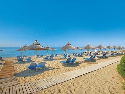 Strand mit Holzsteg, blauen Liegestühlen und strohgedeckten Sonnenschirmen unter blauem Himmel.