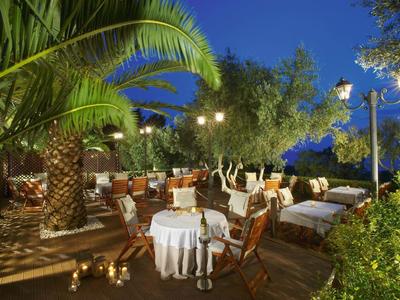 Abendliche Terrasse mit Palmbaum, Tischen mit weißen Tüchern, Holzmöbeln und Lichterketten.