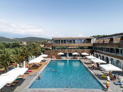 Großer rechteckiger Pool in einem Hotel mit Liegestühlen und Sonnenschirmen, umgeben von einer mediterranen Landschaft.