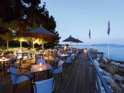 Abendliche Terrasse eines Restaurants am Meer mit beleuchteten Tischen und Blick auf das Wasser.
