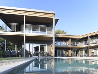 Modernes Hotel mit großem Pool und Balkonen an zwei Gebäudeflügeln unter blauem Himmel.