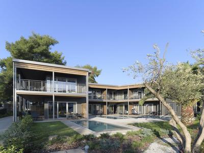 Moderner Hotelkomplex mit Pool, umgeben von Bäumen und klarem Himmel.