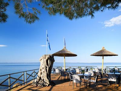 Terrasse mit Tischen, Stühlen und Sonnenschirmen mit Meerblick unter blauem Himmel.