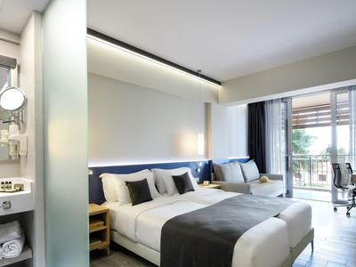 Modernes Hotelzimmer mit zwei großen Betten, grauen Akzenten und Blick auf den Balkon.