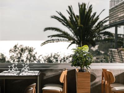 Terrasse mit Tischen und Stühlen, Pflanzen und Meerblick bei bewölktem Himmel.