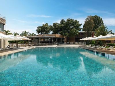Großer Pool mit klar blauem Wasser, umgeben von Liegestühlen und Sonnenschirmen bei klarem Himmel.