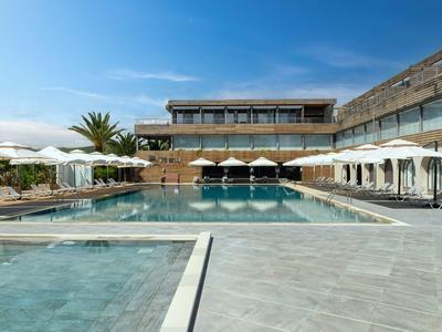 Moderner Hotelpool mit Liegestühlen, Sonnenschirmen und klar blauem Himmel im Hintergrund.