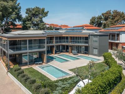 Modernes Hotel mit Pool und Terrasse, umgeben von Bäumen und klarem Himmel.