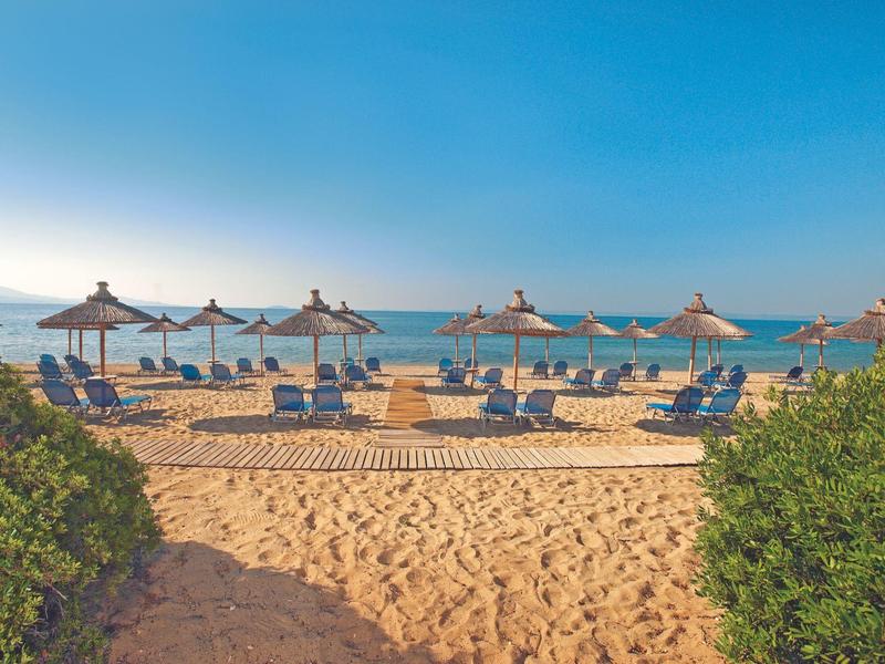 Sandstrand mit blauem Himmel, Liegestühlen und Sonnenschirmen aus Stroh am Meer.