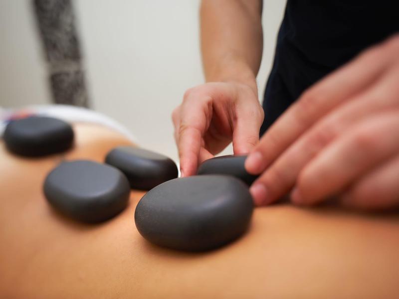 Schwarze Massage-Steine werden auf dem Rücken einer liegenden Person platziert, entspannende Szene.