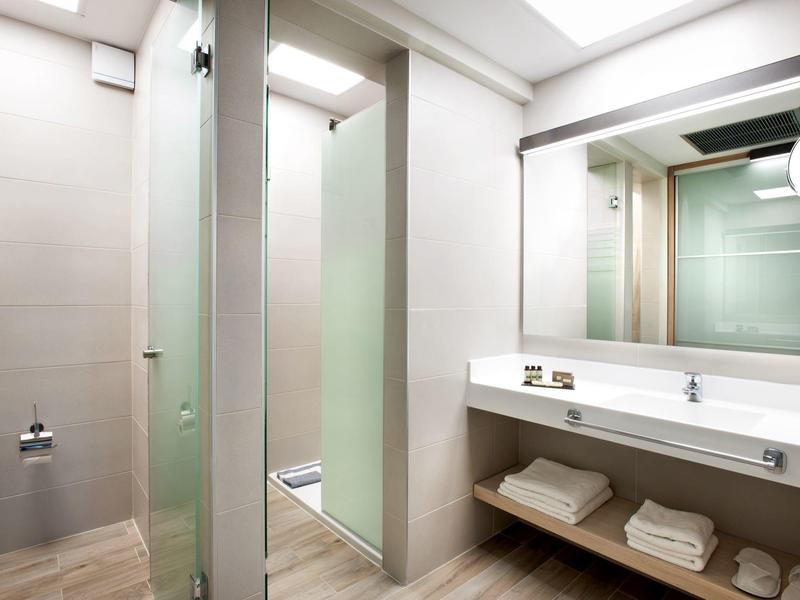 Moderner, heller Badezimmerbereich mit Glas-Dusche, großem Spiegel und weißem Waschbecken.