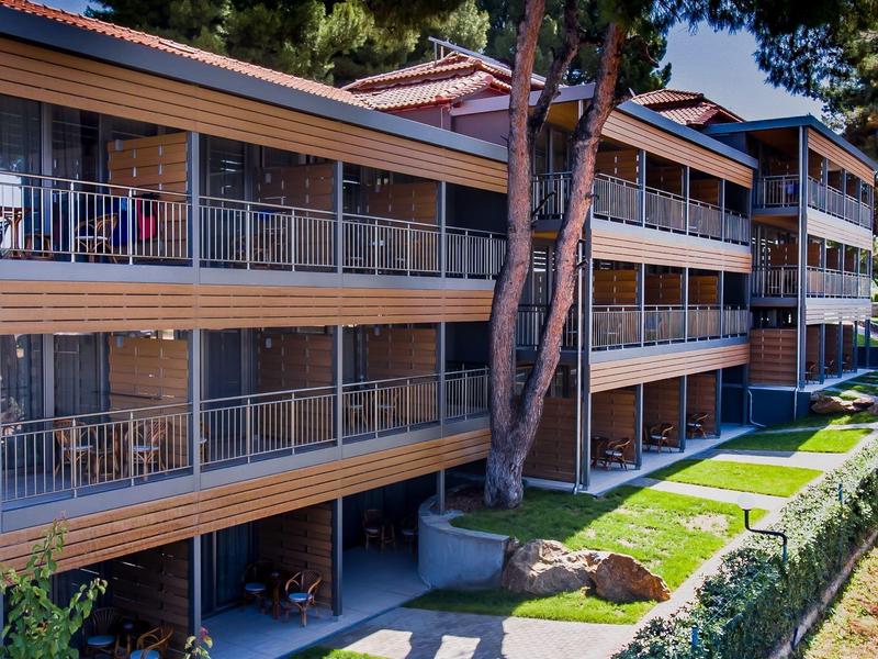 Mehrstöckiges Wohngebäude mit Balkonen, umgeben von Bäumen und Rasenflächen an einem sonnigen Tag.