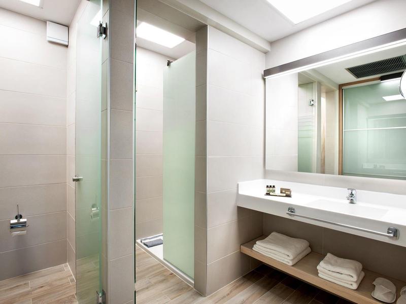 Helles Badezimmer mit Waschbecken, Spiegel, WC, Holzfußboden und frosted Glas-Duschwand.