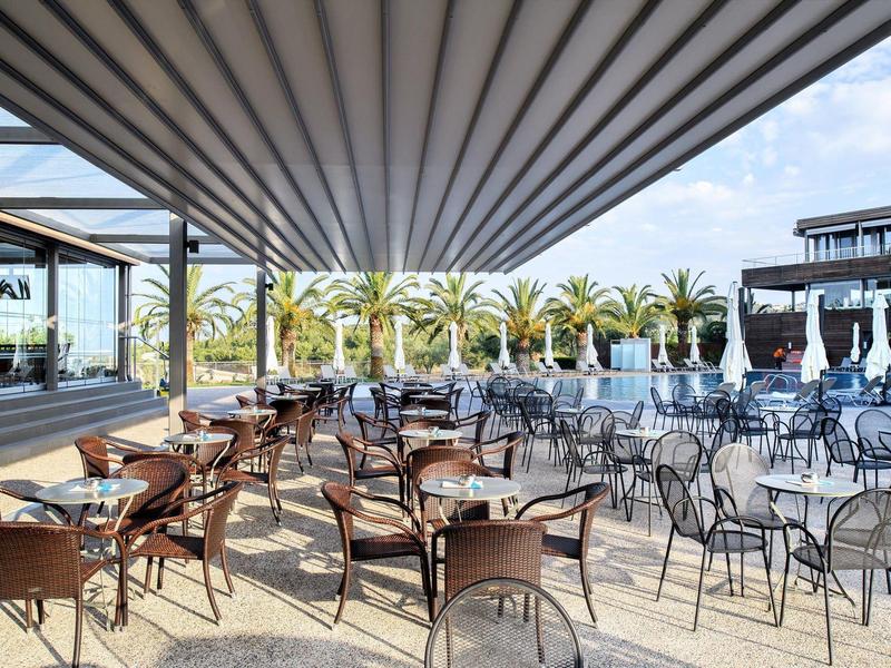 Terrasse mit vielen Stühlen, Tischen, Palmen im Hintergrund und blauem Himmel.