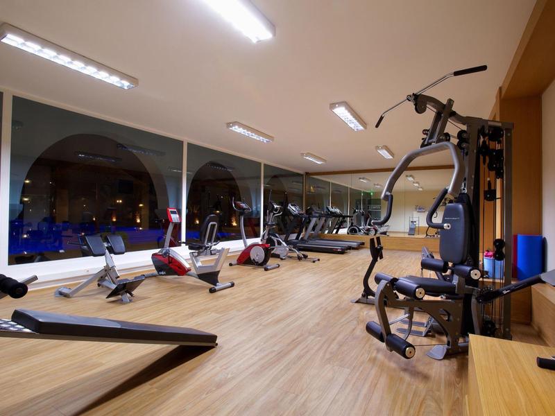 Moderner Fitnessraum mit Holzfußboden, großen Fenstern und verschiedenen Trainingsgeräten.