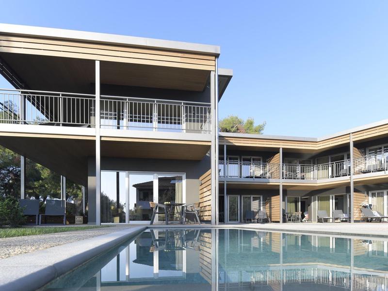 Modernes Gebäude mit zwei Etagen, großen Balkonen und einem großen Schwimmbecken im Vordergrund.