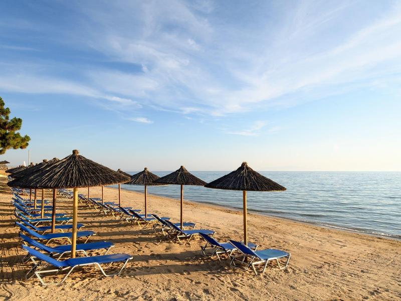 Empty sun loungers with straw roofs on sandy beach under clear sky and calm sea.