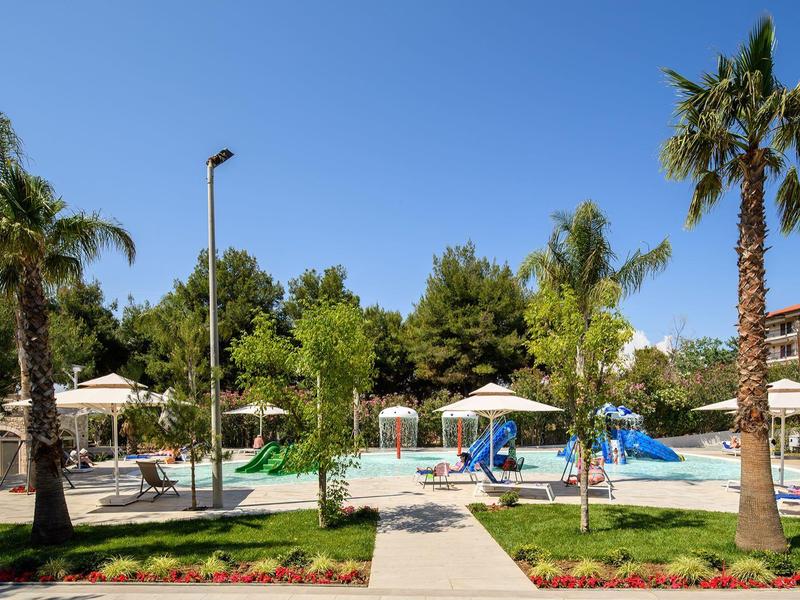 Leisure area with swimming pool, slides, and palm trees under clear blue sky.