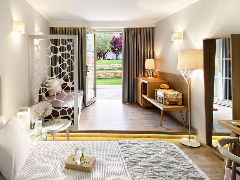 Modern hotel room with double bed, armchair, wardrobe with TV, and garden access.