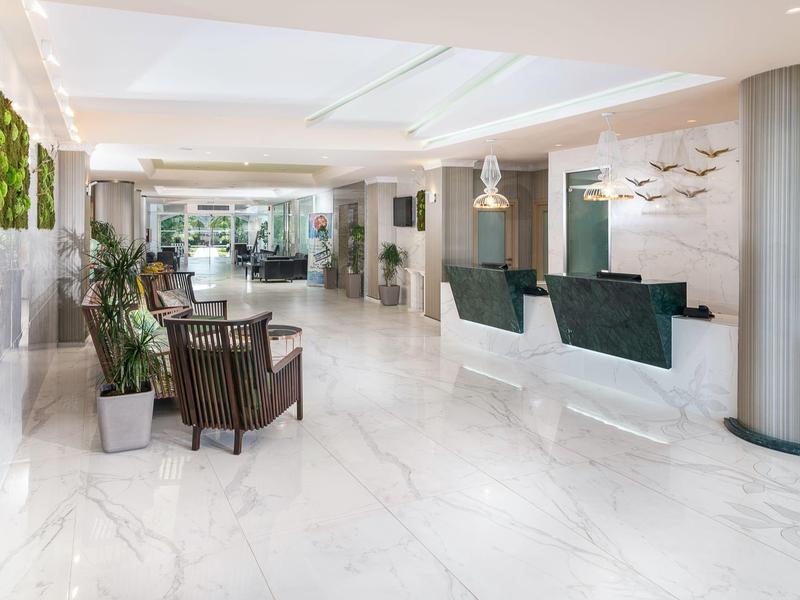 Modern hotel lobby with white marble floor, reception desk, and seating area.