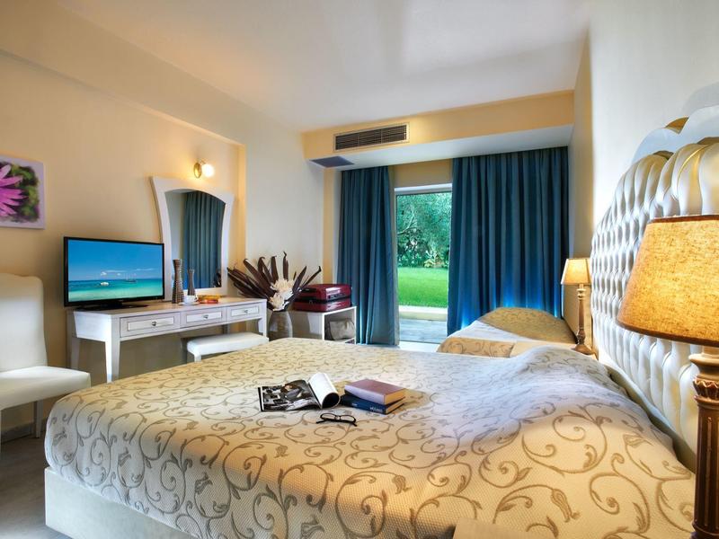 Bright hotel room with large bed, desk, TV, and garden view.