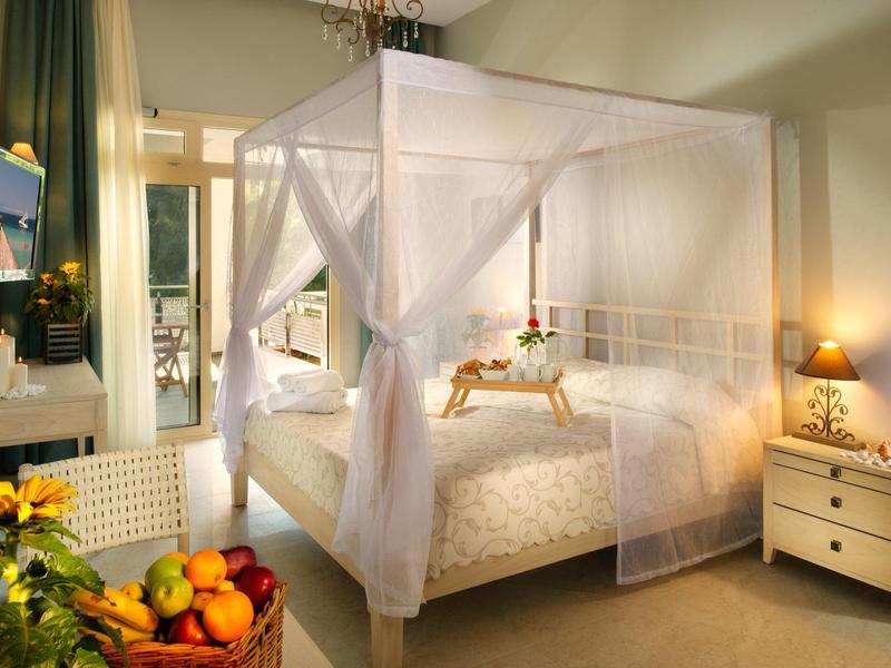 Cozy hotel room with canopy bed, nightstand, and fruit basket by the window.