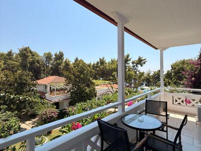 Balkon s stolem a čtyřmi židlemi, převážně bílý, s výhledem na zelené stromy a budovy.