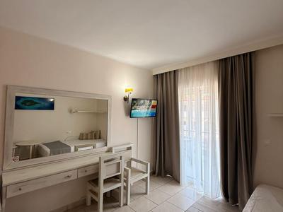 Lichte hotelkamer met bureau, stoelen, tv en groot raam met gordijnen.