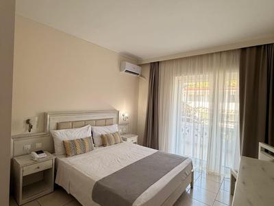 Lichte hotelkamer met tweepersoonsbed, nachtkastjes en balkon deur met gordijnen.